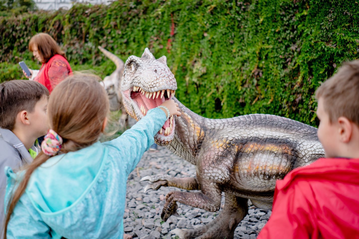 child putting her arm on a dinosaur s mouth